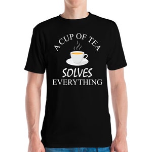 Może przedstawiać: Czarna koszulka z białym napisem "A CUP OF TEA SOLVES EVERYTHING". Nad tekstem znajduje się grafika białego kubka z herbatą z żółtym płynem i parą. Kubek stoi na białym spodku.