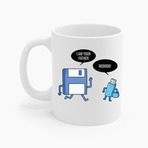 Könnte beinhalten: Weiße Keramik-Tasse mit einem humorvollen Cartoon-Design. Das Design zeigt einen blauen Disketten-Charakter, der "I AM YOUR FATHER" zu einem blauen USB-Stick-Charakter sagt, der mit "NOOOOOO!" antwortet.