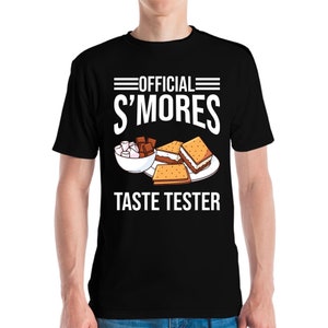 May include: Black t-shirt featuring the text "OFFICIAL S'MORES TASTE TESTER" in white. The design includes a bowl of marshmallows, chocolate pieces, and s'mores on a plate. A casual tee for s'mores enthusiasts.