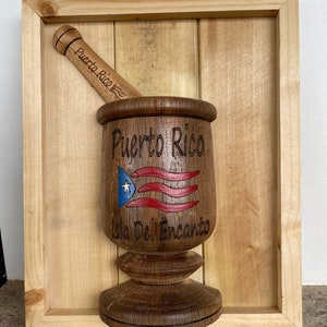 May include: A wooden mortar and pestle set with the words "Puerto Rico" and "Isla Del Encanto" carved into the side. The mortar is decorated with a red, white, and blue Puerto Rican flag.