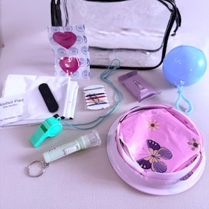 May include: A clear, zippered travel bag filled with various items, including a blue balloon, a whistle, a small flashlight, and a pink container with a butterfly design. Other items include a nail file, alcohol pads, and hair ties.