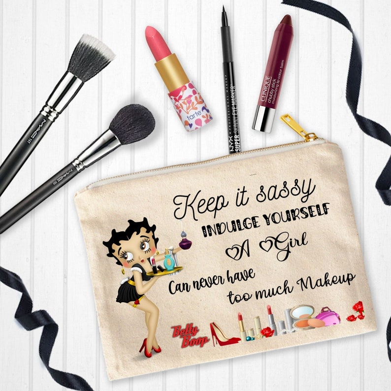 May include: A beige canvas makeup bag with a zipper closure. The bag features a cartoon image of Betty Boop holding a tray of makeup. The text on the bag reads "Keep it sassy Indulge yourself A Girl Can never have too much Makeup".