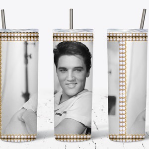 May include: A stainless steel tumbler featuring a black and white image of Elvis Presley. The tumbler has a gold and white decorative border with a silver straw. The design wraps around the entire tumbler.