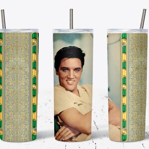 May include: A stainless steel tumbler featuring a portrait of Elvis Presley on one side and a decorative gold and green pattern on the other. The tumbler has a silver straw and a clear lid. The design is a tribute to the iconic singer.