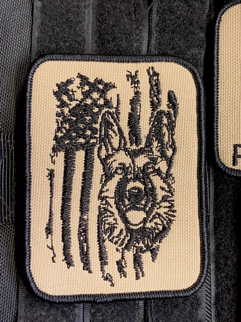 May include: A tan embroidered patch with a black German Shepherd dog silhouette in front of an American flag.