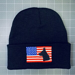 May include: Black knit beanie with a red, white, and blue American flag patch featuring a silhouette of a German Shepherd dog.