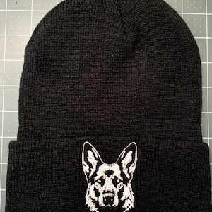 May include: Black knit beanie with a white embroidered German Shepherd dog head on the front.