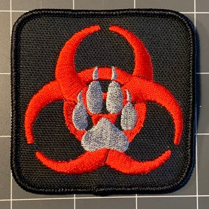 May include: A black embroidered patch with a red biohazard symbol and a gray paw print in the center.