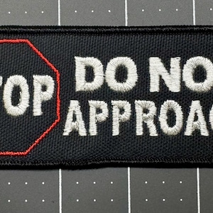 May include: A rectangular black embroidered patch with rounded corners. On the left, a red-outlined octagon contains the white embroidered text STOP. To the right, the white embroidered text DO NOT APPROACH is displayed in capital letters.