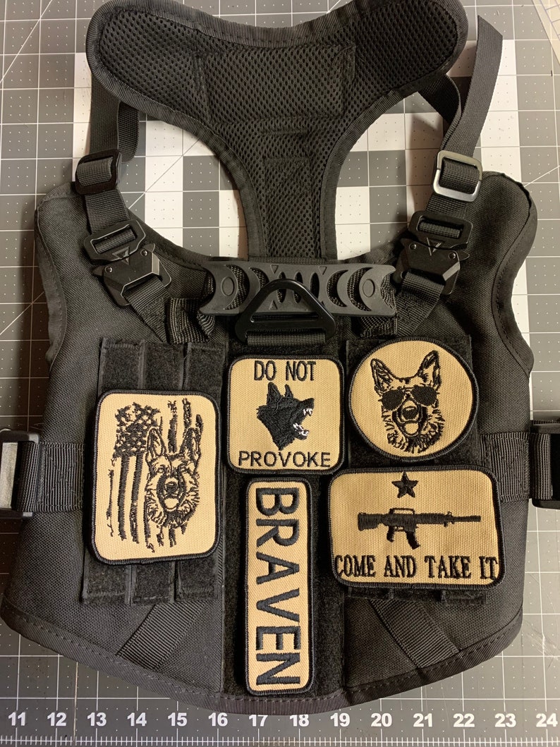 May include: Black tactical dog harness with multiple patches. The patches include a dog silhouette with the text "Do Not Provoke", a dog with sunglasses, a dog with an American flag, a patch with the text "Braven", and a patch with a rifle and the text "Come and Take It".