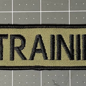 May include: A green and black rectangular patch with the text "IN TRAINING" embroidered in black.