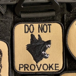 May include: A tan patch with black embroidered text and a black embroidered image of a dog's head. The text reads "DO NOT PROVOKE".