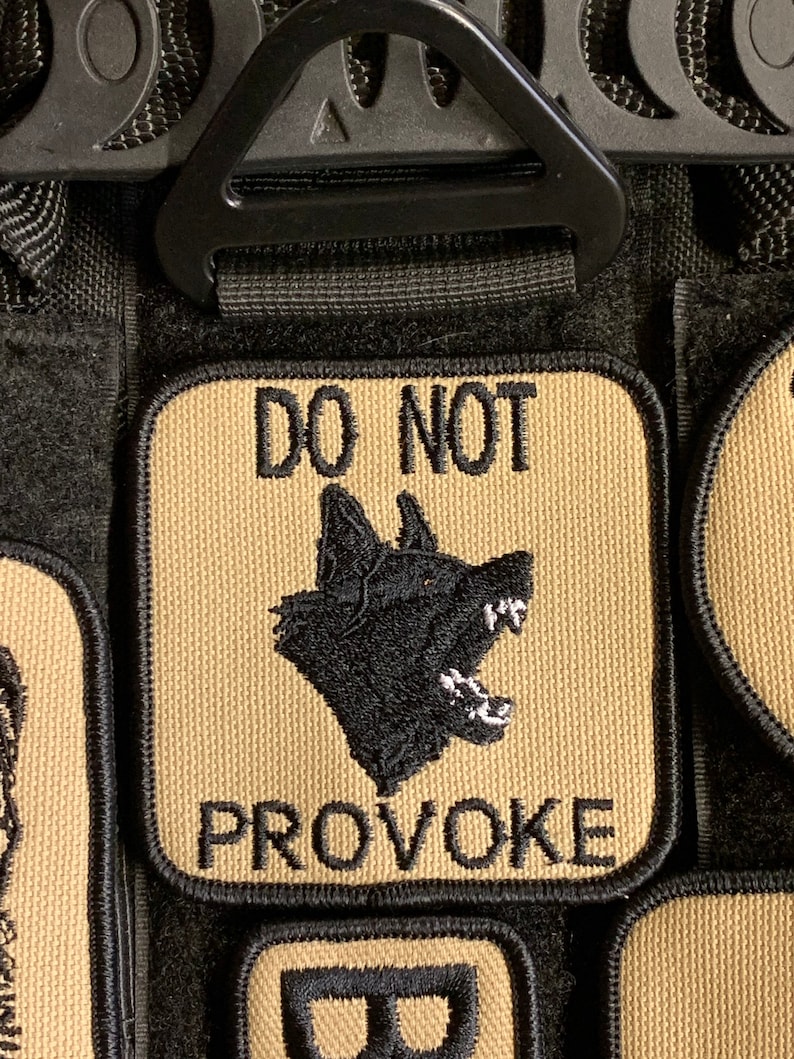 May include: A tan patch with black embroidered text and a black embroidered image of a dog's head. The text reads "DO NOT PROVOKE".