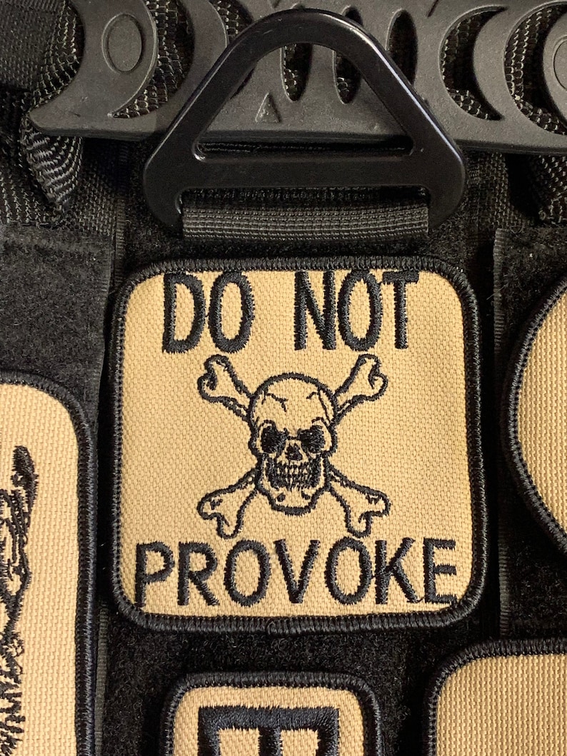May include: A tan patch with black embroidered text that reads "DO NOT PROVOKE" and a skull and crossbones design.