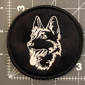 May include: White embroidered German Shepherd dog head silhouette on a black circular patch.