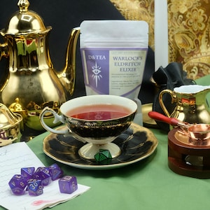 May include: A teacup filled with tea sits on a saucer, next to a bag of "Warlock's Eldritch Elixir" tea. A gold teapot, creamer, and sugar bowl are also present. Purple dice and a green die are on the table.