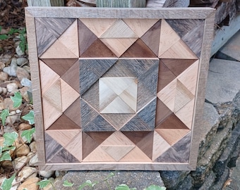 May include: A framed geometric wall art piece made of wood with a variety of wood tones, including brown, gray, and light wood. The wood pieces are arranged in a pattern of triangles and squares.