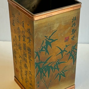 May include: A square, brass vase with a copper rim. The vase has a gold background with a green bamboo design and Chinese calligraphy.