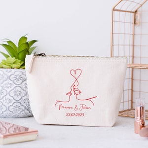 Puede incluir: Bolsa de lona blanca con cremallera con un dibujo de l&iacute;nea roja de dos personas bes&aacute;ndose con un coraz&oacute;n encima. El texto "Marine & Julien 23.07.2023" est&aacute; impreso debajo del dibujo.