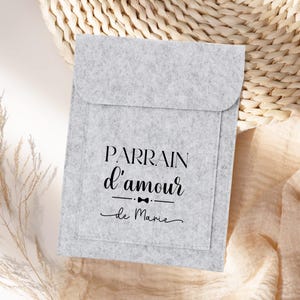 Op de afbeelding: Een grijze gevoerde tas met de tekst "PARRAIN d'amour de Marie" in zwart gedrukt. De tas heeft een klein strikje boven de tekst.