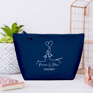 Puede incluir: Una bolsa de maquillaje azul marino con cremallera con un dibujo de l&iacute;nea blanca de dos caras bes&aacute;ndose con un coraz&oacute;n encima. El texto "Marine & Julien 23.07.2023" est&aacute; impreso debajo del dibujo.
