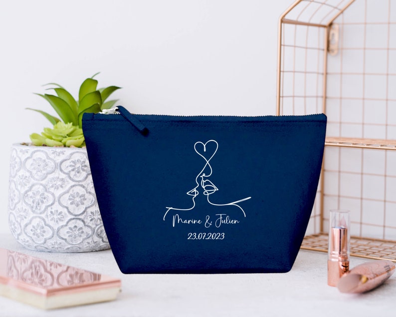 Puede incluir: Una bolsa de maquillaje azul marino con cremallera con un dibujo de l&iacute;nea blanca de dos caras bes&aacute;ndose con un coraz&oacute;n encima. El texto "Marine & Julien 23.07.2023" est&aacute; impreso debajo del dibujo.