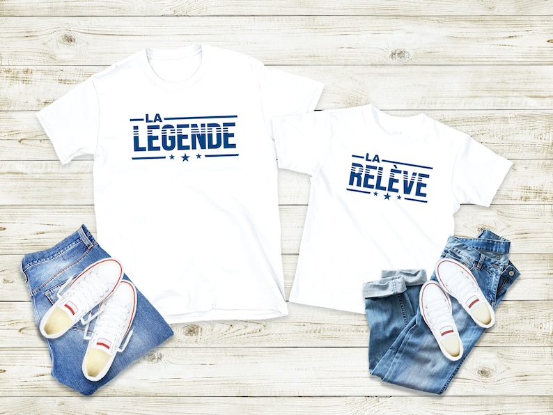 Peut inclure: Deux t-shirts blancs avec du texte bleu. Le plus grand t-shirt dit "LA LEGENDE" et le plus petit dit "LA RELEVE". Les deux t-shirts ont trois &eacute;toiles sous le texte.