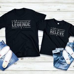 Peut inclure: Deux t-shirts noirs avec un imprim&eacute; graphique blanc. Le plus grand t-shirt dit "LA LEGENDE" avec trois &eacute;toiles. Le plus petit t-shirt dit "LA RELEVE" avec trois &eacute;toiles.
