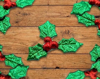 May include: Green holly leaves with red berries arranged on a wooden background. The leaves have a textured, metallic finish, and the berries are shiny. The arrangement suggests a festive, holiday theme.