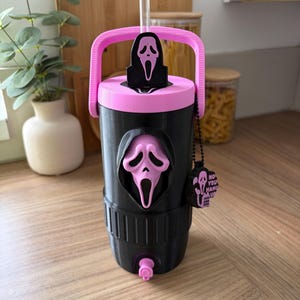 May include: A black and pink tumbler with a Ghostface mask emblem on the front and lid. The cup features a pink handle, a clear straw, and a small black charm attached by a chain that reads "NO YOU HANG UP" with a small phone icon and mask graphic.