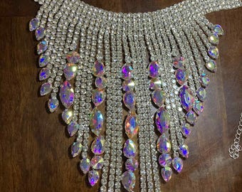 May include: A dazzling silver rhinestone necklace with a cascading fringe design. The necklace features rows of small, sparkling rhinestones and larger, iridescent teardrop-shaped gems. The design is symmetrical and eye-catching, perfect for special occasions.