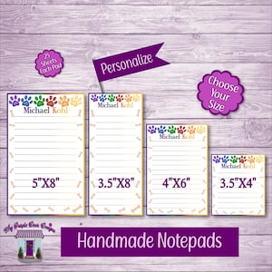 May include: Four different sizes of personalized notepad paper with a paw print design. The notepads are 5 inches by 8 inches, 3.5 inches by 8 inches, 4 inches by 6 inches, and 3.5 inches by 4 inches. The notepads are white with a rainbow paw print design and a yellow border. The notepads are personalized with the name "Michael Kohl".