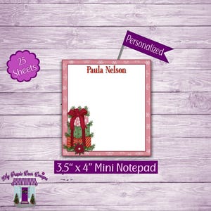 May include: A pink and white notepad with a Christmas theme. The notepad has a stack of presents with a red bow on top. The notepad is 3.5 inches by 4 inches and has 25 sheets. The text "Paula Nelson" is at the top of the notepad. The text "Personalized" is on a purple flag.