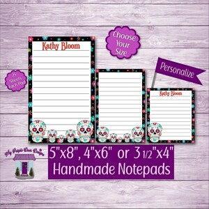 May include: Three personalized notepad designs with a Day of the Dead theme. The notepads feature a black and white border with colorful sugar skulls and flowers. The notepads are available in three sizes: 5 inches by 8 inches, 4 inches by 6 inches, and 3 1/2 inches by 4 inches.