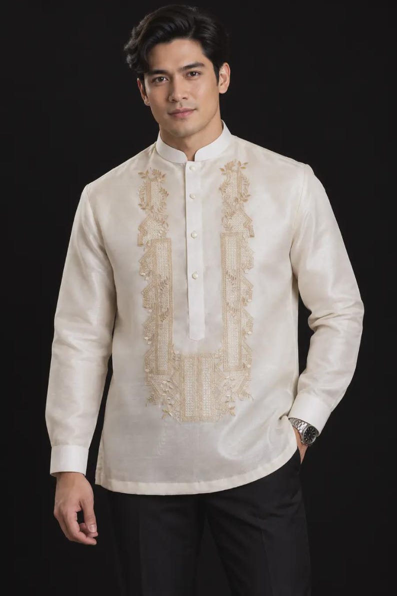 May include: A long-sleeved, off-white Barong Tagalog shirt featuring a mandarin collar, a partial button-down front, and intricate, symmetrical gold-toned embroidery panels running down the chest. The fabric has a subtle, semi-sheer sheen.