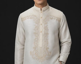 May include: A long-sleeved, off-white barong tagalog shirt featuring a mandarin collar and a button-down placket. The garment is adorned with intricate, light gold-colored embroidery across the chest and collar, showcasing a detailed floral pattern.