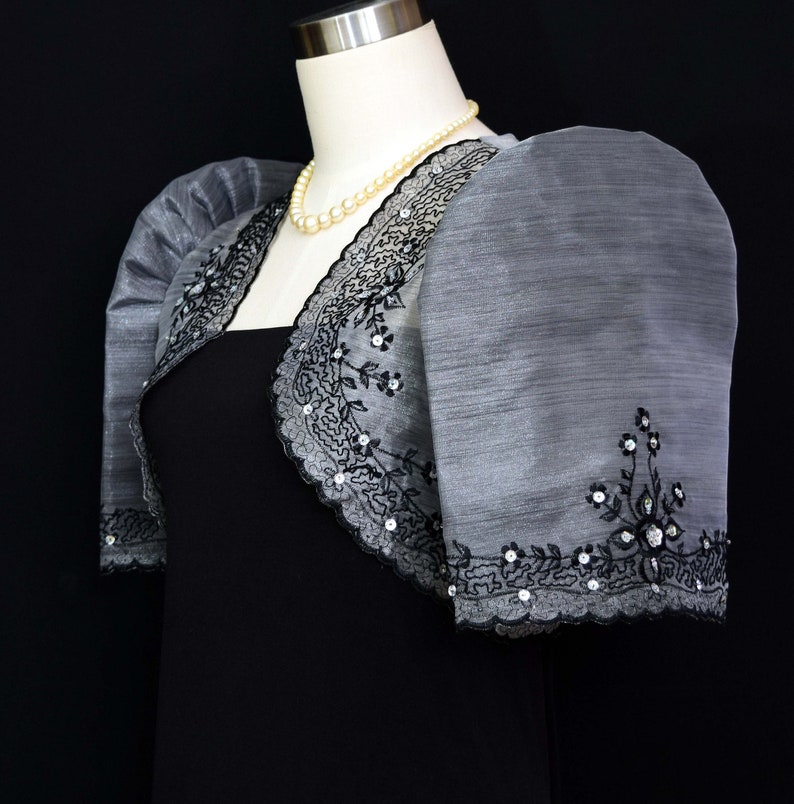 Our Silver/Black Traje de Mestiza Embroidered Bolero is a testament to understated beauty. Crafted from  Organza fabric, with a butterfly sleeves, delicate floral design & a refined standing collar that adds  a touch of timeless charm to any occasion