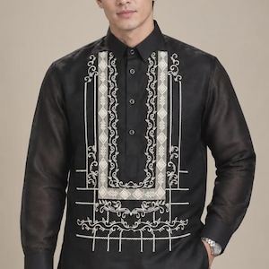May include: A black long-sleeved button-down shirt featuring a sheer fabric and intricate white embroidery along the front placket and chest. The design includes geometric patterns and floral vine motifs, with a classic collar and buttoned cuffs.