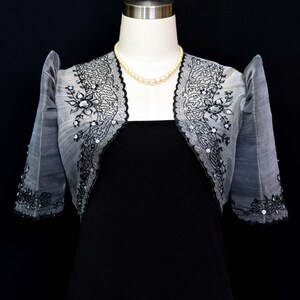 Our Silver/Black Traje de Mestiza Embroidered Bolero is a testament to understated beauty. Crafted from  Organza fabric, with a butterfly sleeves, delicate floral design & a refined standing collar that adds  a touch of timeless charm to any occasion