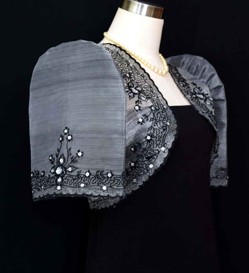 Our Silver/Black Traje de Mestiza Embroidered Bolero is a testament to understated beauty. Crafted from  Organza fabric, with a butterfly sleeves, delicate floral design & a refined standing collar that adds  a touch of timeless charm to any occasion