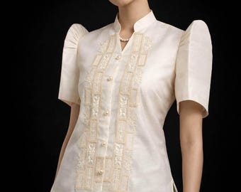 May include: An off-white short-sleeved blouse featuring a mandarin collar, structured puff sleeves, and a front button closure with pearl-like buttons. The bodice is decorated with vertical panels of intricate cream-colored embroidery.
