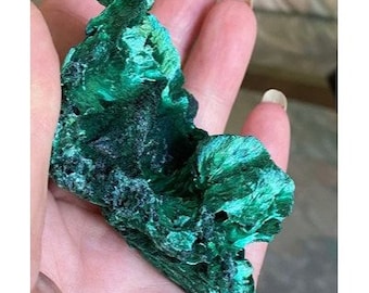 May include: A large, green malachite crystal with a rough, textured surface. The crystal has a unique, organic shape and is a beautiful example of this mineral.
