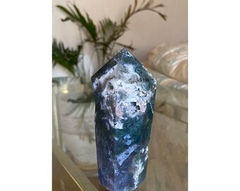 May include: A green and white agate crystal point with a polished finish. The crystal is a natural stone with a unique pattern of green, white, and gray.