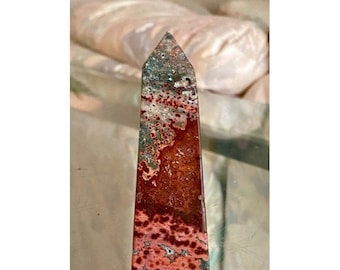 May include: A red, brown, and green agate obelisk with a pointed top. The obelisk has a swirling pattern of colors and white speckles.