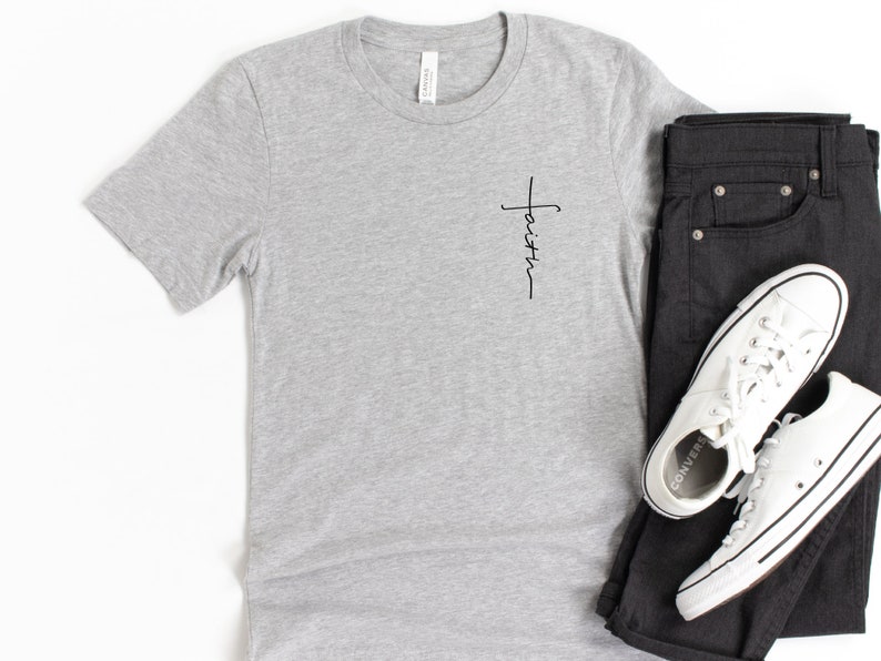 May include: A gray t-shirt with a small black cross and the word "faith" written vertically on the left side of the chest.