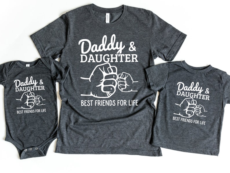May include: Three gray shirts with white text that reads "Daddy & Daughter Best Friends For Life" and a fist bump graphic. The shirts are in different sizes, one is a baby onesie.