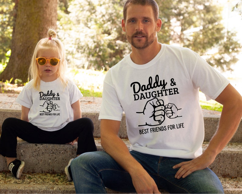 May include: White t-shirts with black text and a graphic of two fists bumping. The text reads "Daddy & Daughter Best Friends For Life".