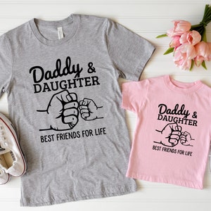 May include: Two gray and pink t-shirts with a black graphic of two fists bumping. The text on the shirts reads "Daddy & Daughter Best Friends For Life".