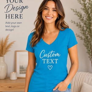 A woman wearing a blue t-shirt with the text "Custom Text" and a heart symbol stands in a room with a wooden table and a plant.
