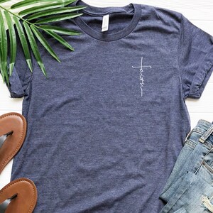 May include: A navy blue t-shirt with a white cross and the word "faith" written vertically on the front.